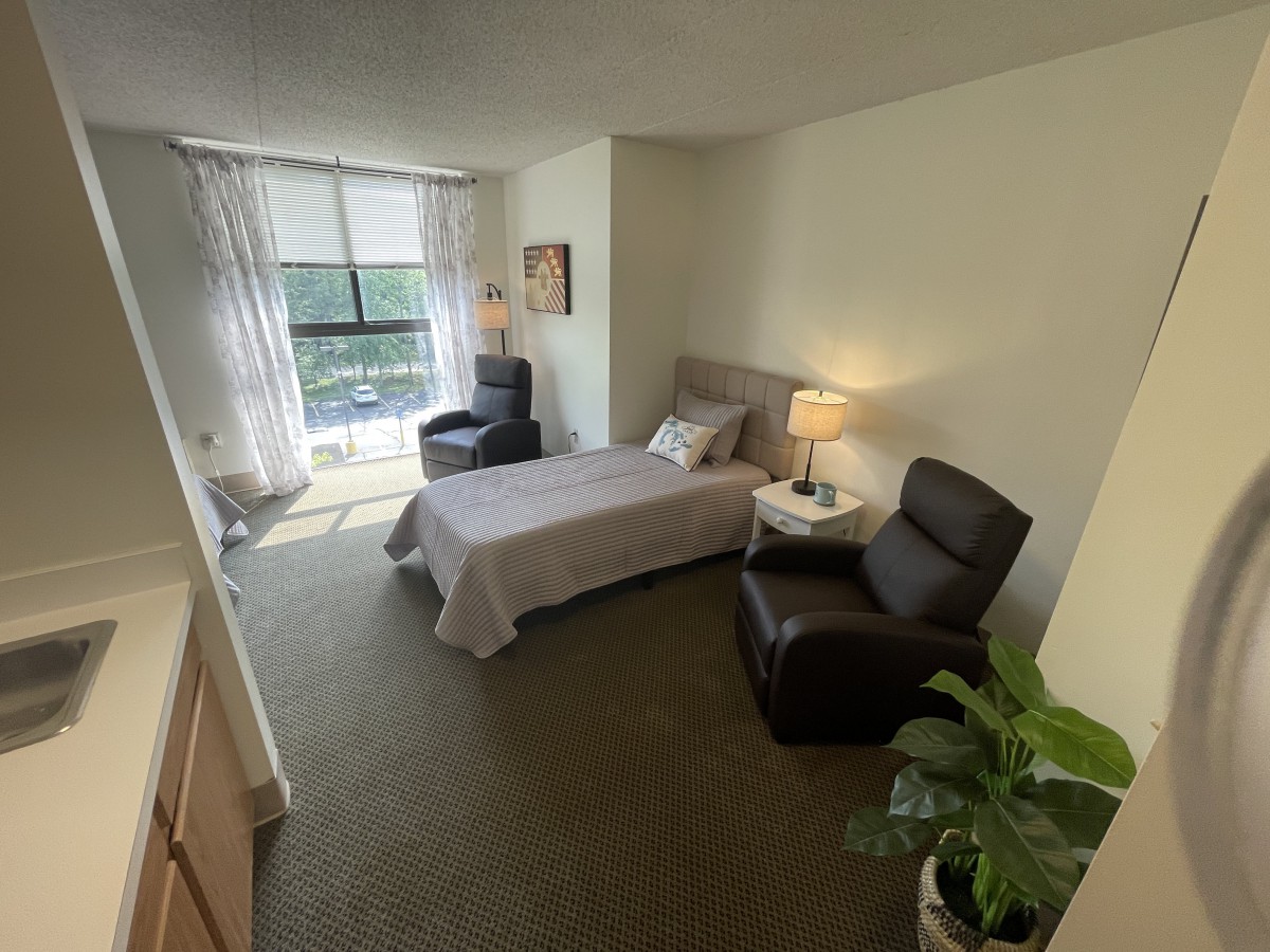 A cozy bedroom with a single bed, armchair, and large window letting in natural light.