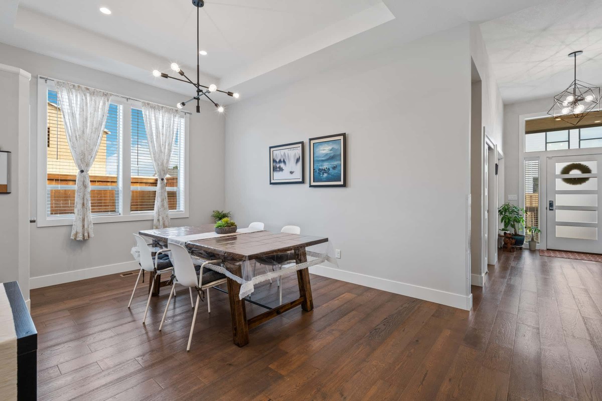 A modern dining room featuring a wooden table, contemporary chandelier, and ample natural light.