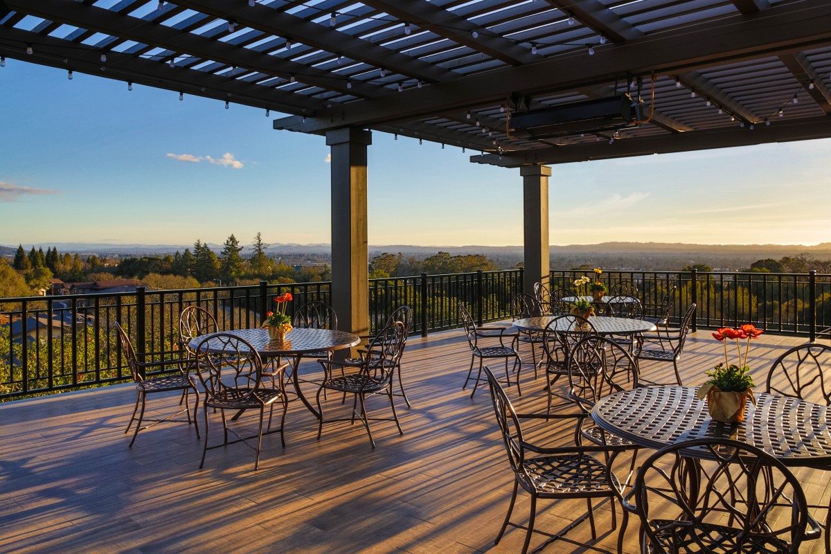 A beautiful outdoor patio with wrought iron tables and chairs under a pergola, offering a scenic sunset view.