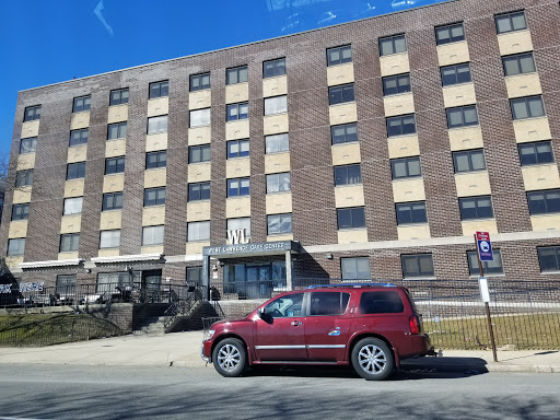 A red car parked in front of a multistory brick apartment building.