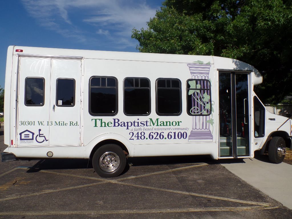 A shuttle bus from The Baptist Manor is parked in a parking lot.