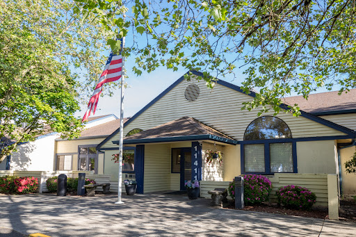 A charming community center with an American flag waving in front, surrounded by lush greenery.