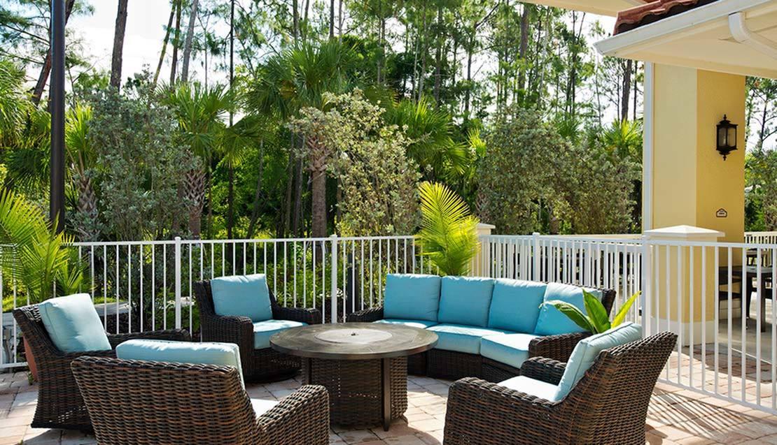 An inviting outdoor patio with wicker furniture and blue cushions, surrounded by lush greenery.