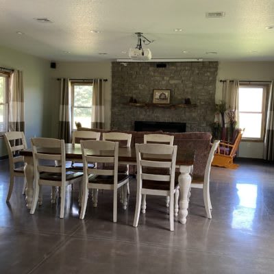 A spacious dining room with a large table and chairs, featuring a stone fireplace and multiple windows.