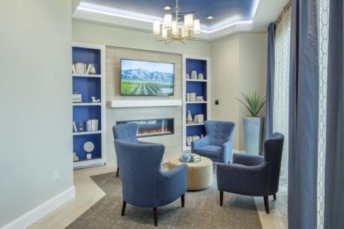 A modern living room with blue chairs and a fireplace, featuring built-in bookshelves and elegant decor.