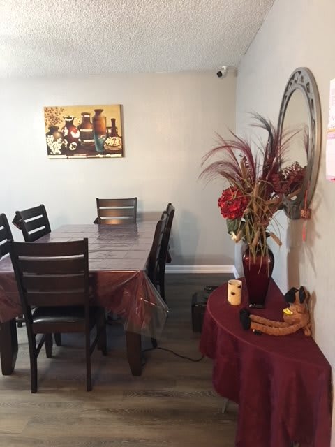 A cozy dining room with a long table, chairs, wall art, and decorative elements such as a mirror and vase with flowers.
