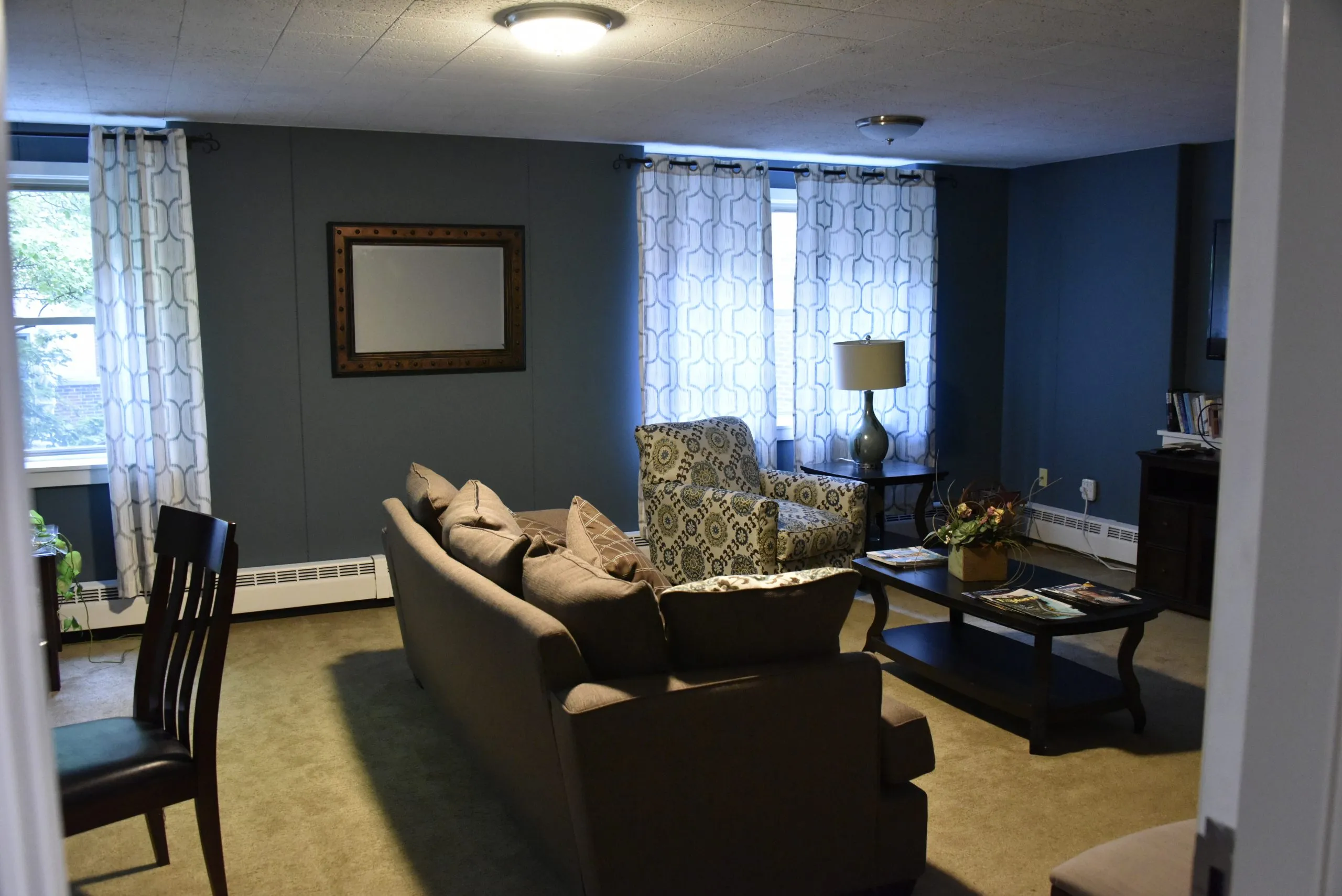 A cozy living room with a sofa, armchair, coffee table, and decorative elements like wall art and curtains.