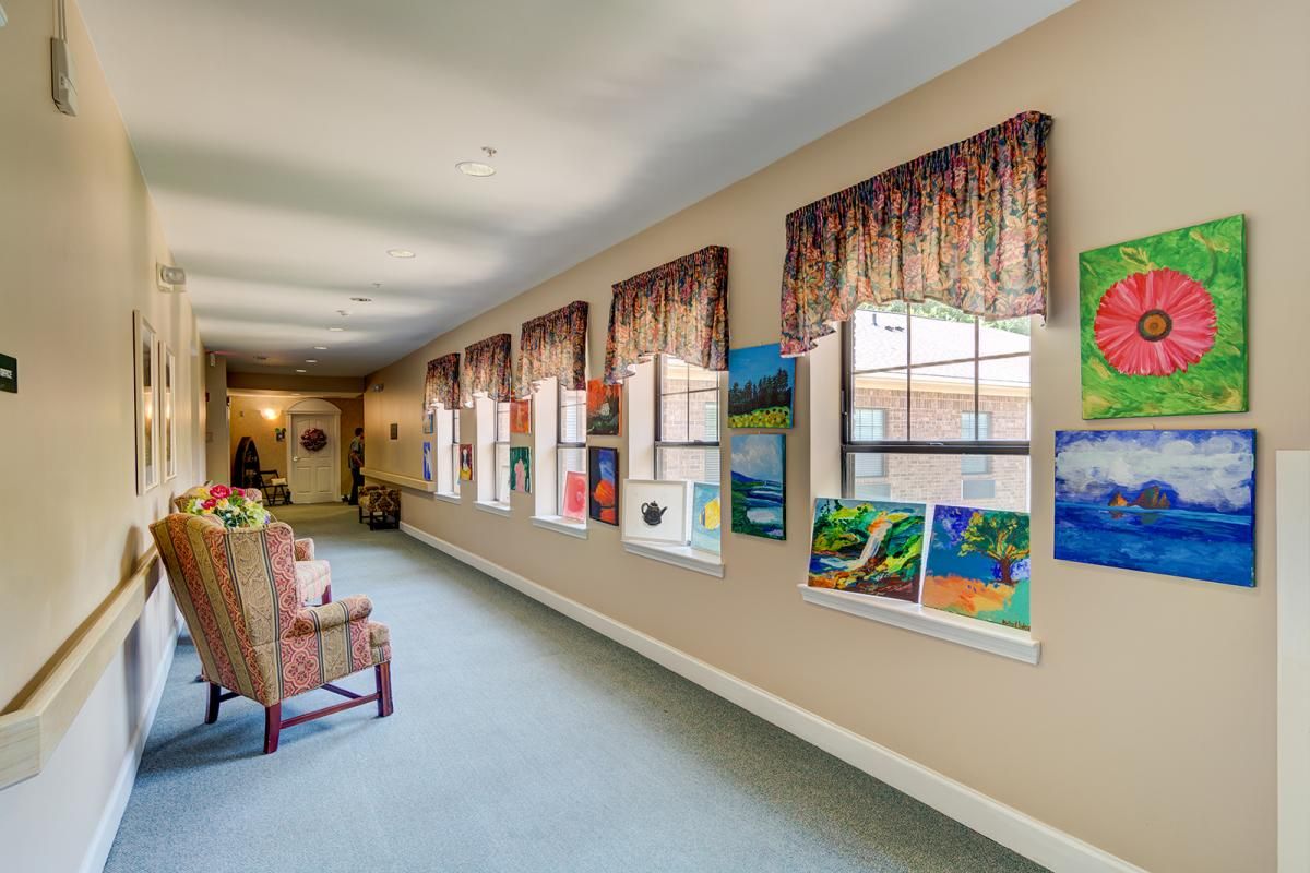 A hallway adorned with vibrant artwork and lined with windows, featuring comfortable chairs and elegant curtains.