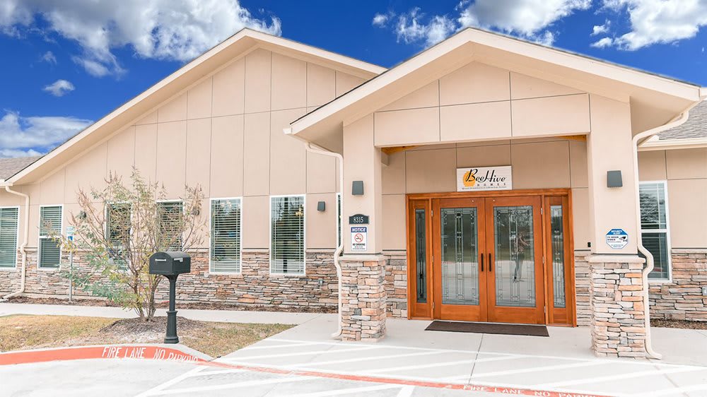 A modern commercial building with a stone facade and large glass doors under a partly cloudy sky.