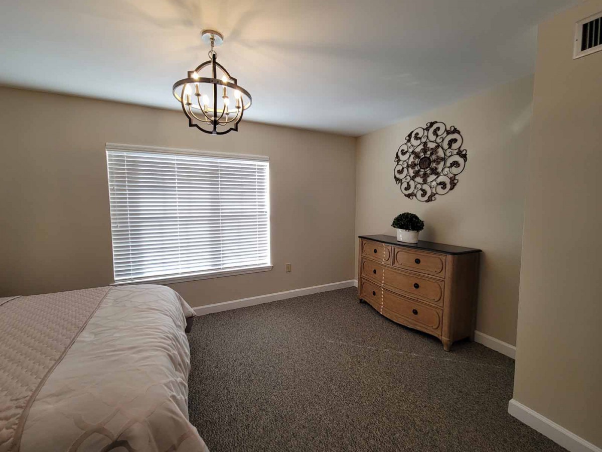 A modern bedroom with a chandelier, dresser, and a large window.
