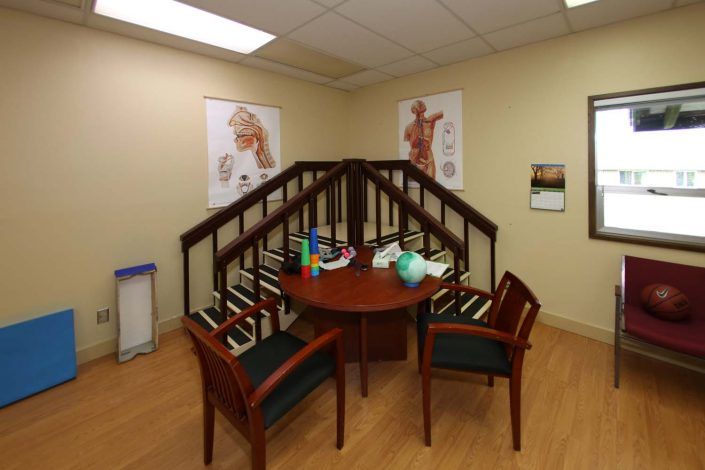 A small meeting room with a round table surrounded by chairs, anatomy posters on the walls, and shelves filled with books.