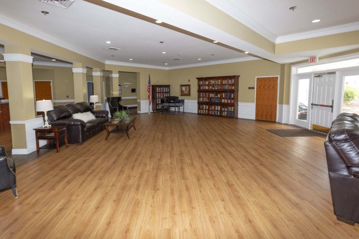 A spacious room with wooden floors, featuring a sofa, a bookshelf, and a piano.