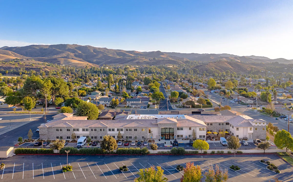 Aerial view of a suburban area with buildings, a parking lot, and surrounding hills.