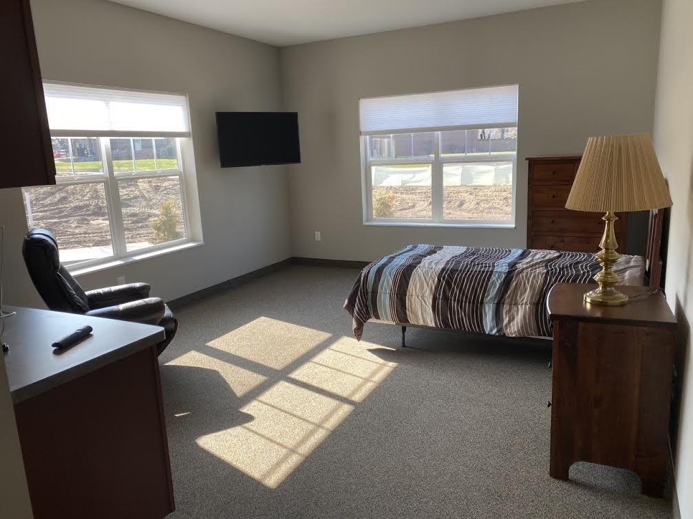A minimalist bedroom with a single bed, television, and ample sunlight streaming through the windows.