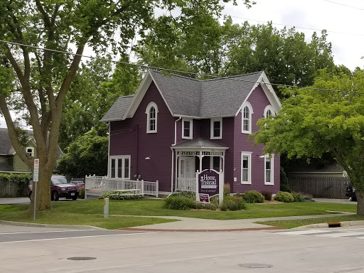 A charming two-story purple house surrounded by greenery in a residential neighborhood.