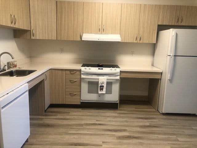 A modern kitchen with wood cabinets, featuring a stove, refrigerator, and dishwasher.