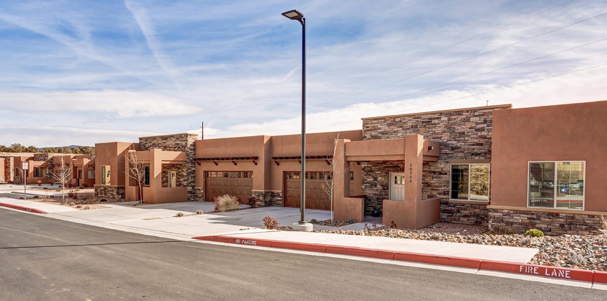 A modern desert-style house with a stone facade and outdoor lighting, viewed from the street.