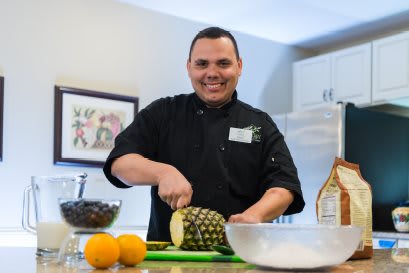 A chef smiling while cutting a pineapple in the kitchen.