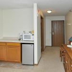 A cozy interior space featuring a kitchenette with wooden cabinets, a microwave, and a small fridge next to a hallway.