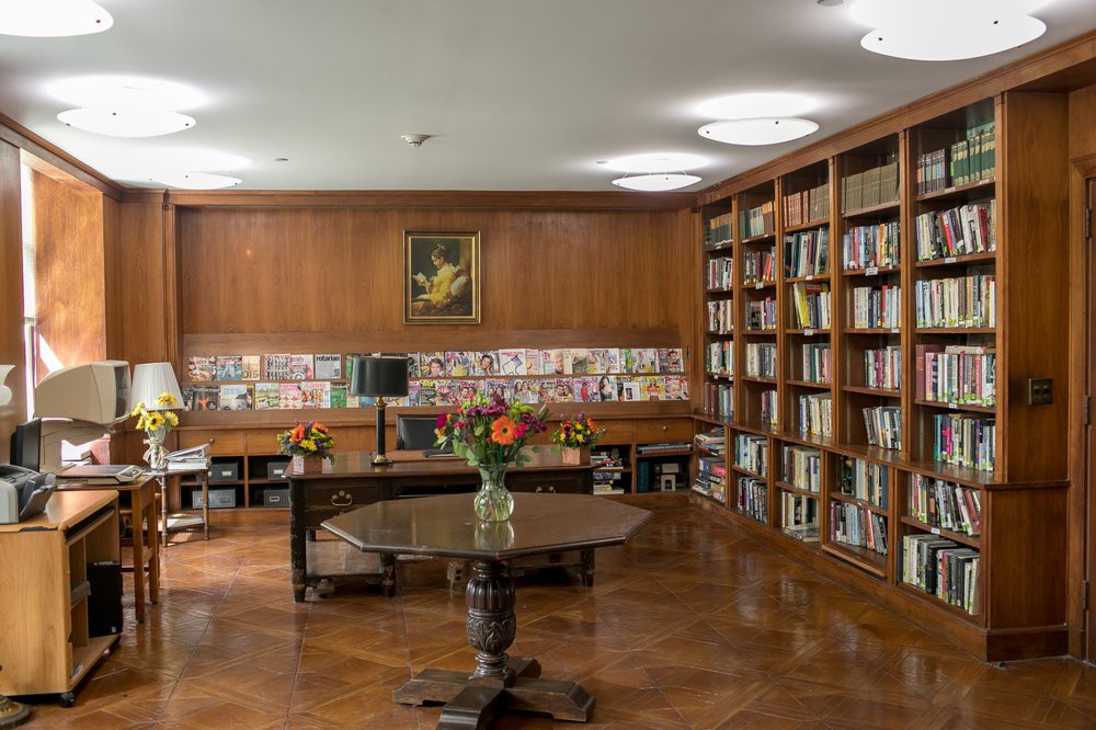 A cozy library room with wooden bookshelves and a central table adorned with flowers, creating an inviting atmosphere for reading and study.