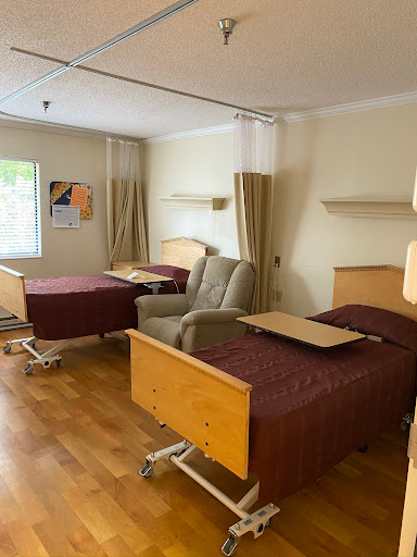 A view of a hospital patient room featuring two adjustable beds and a recliner.