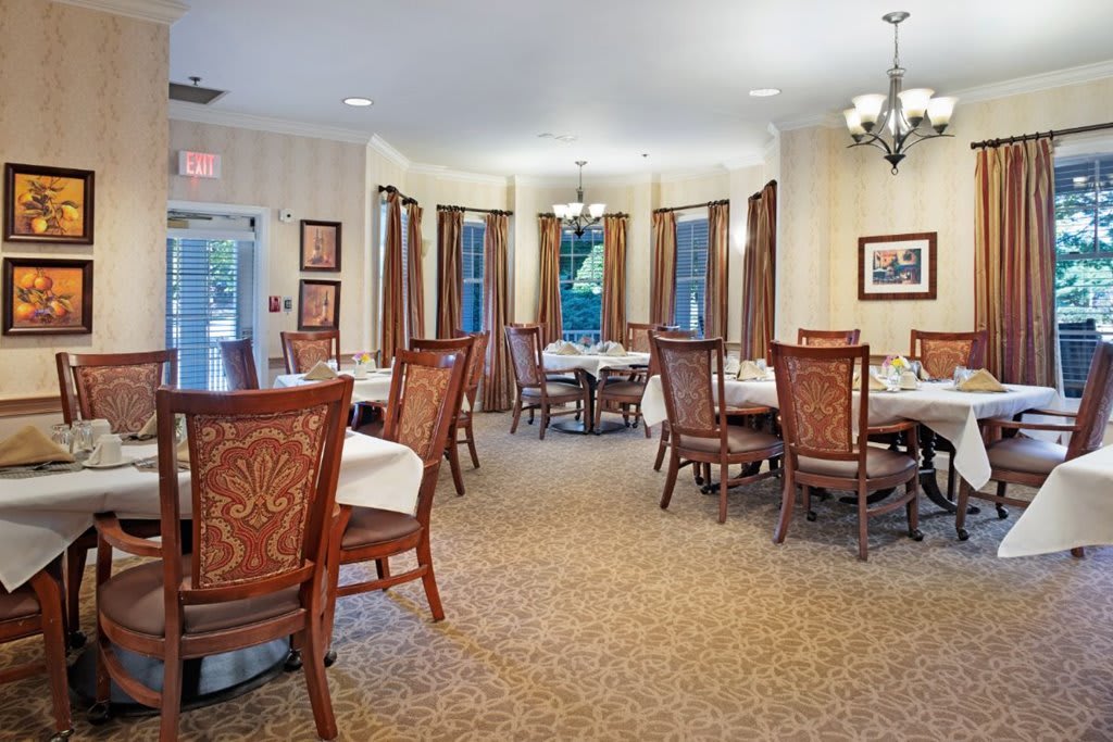 An elegant dining room with neatly arranged tables and chairs, featuring large windows and a chandelier.