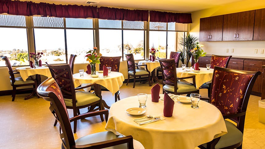 A well-lit restaurant dining room with elegantly set tables and large windows offering a scenic view.