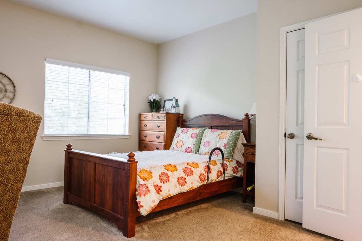 A cozy bedroom with a wooden bed frame, floral quilt, and a window allowing natural light.