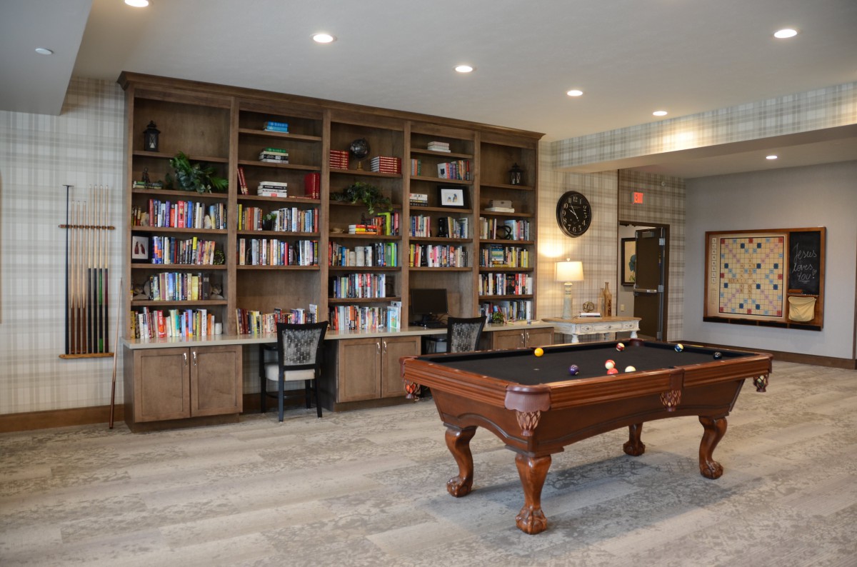 A cozy library room with wooden bookshelves and a billiard table.