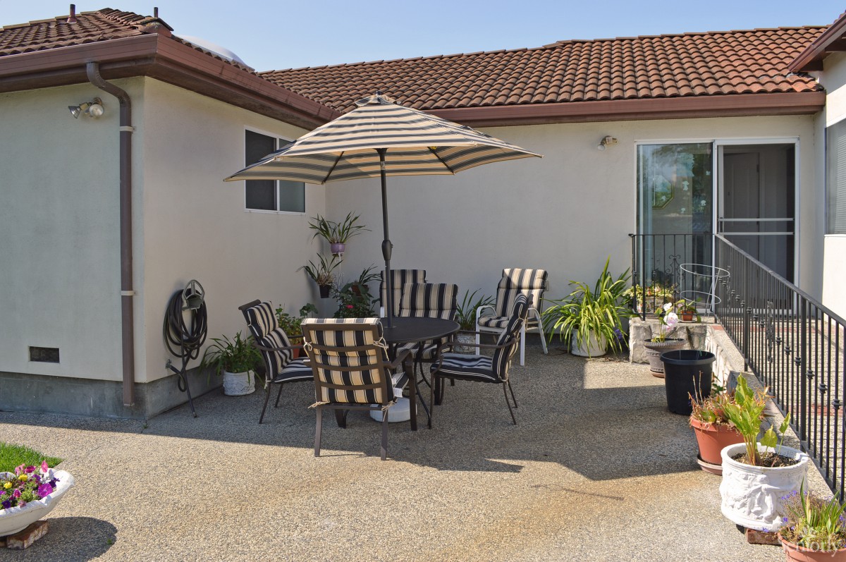 A cozy backyard patio with striped chairs and an umbrella for shade.