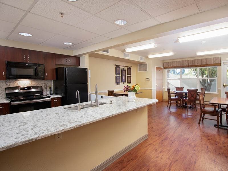 A modern open-concept kitchen and living area with a granite countertop, hardwood flooring, and dining table.