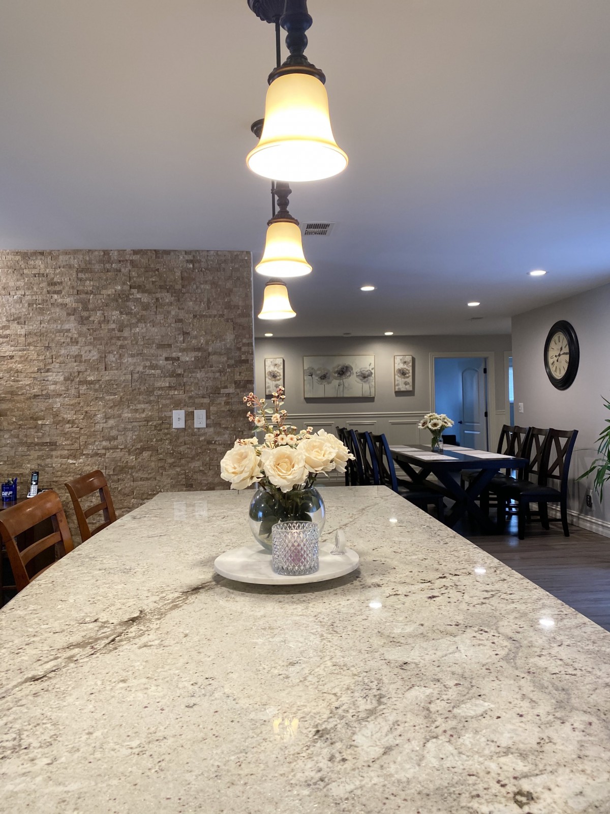 A modern kitchen with a granite countertop and decorative flowers, overlooking a dining area with ambient lighting.