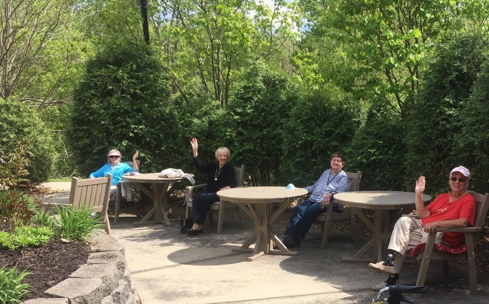 A group of people relaxing on a sunny patio surrounded by trees.