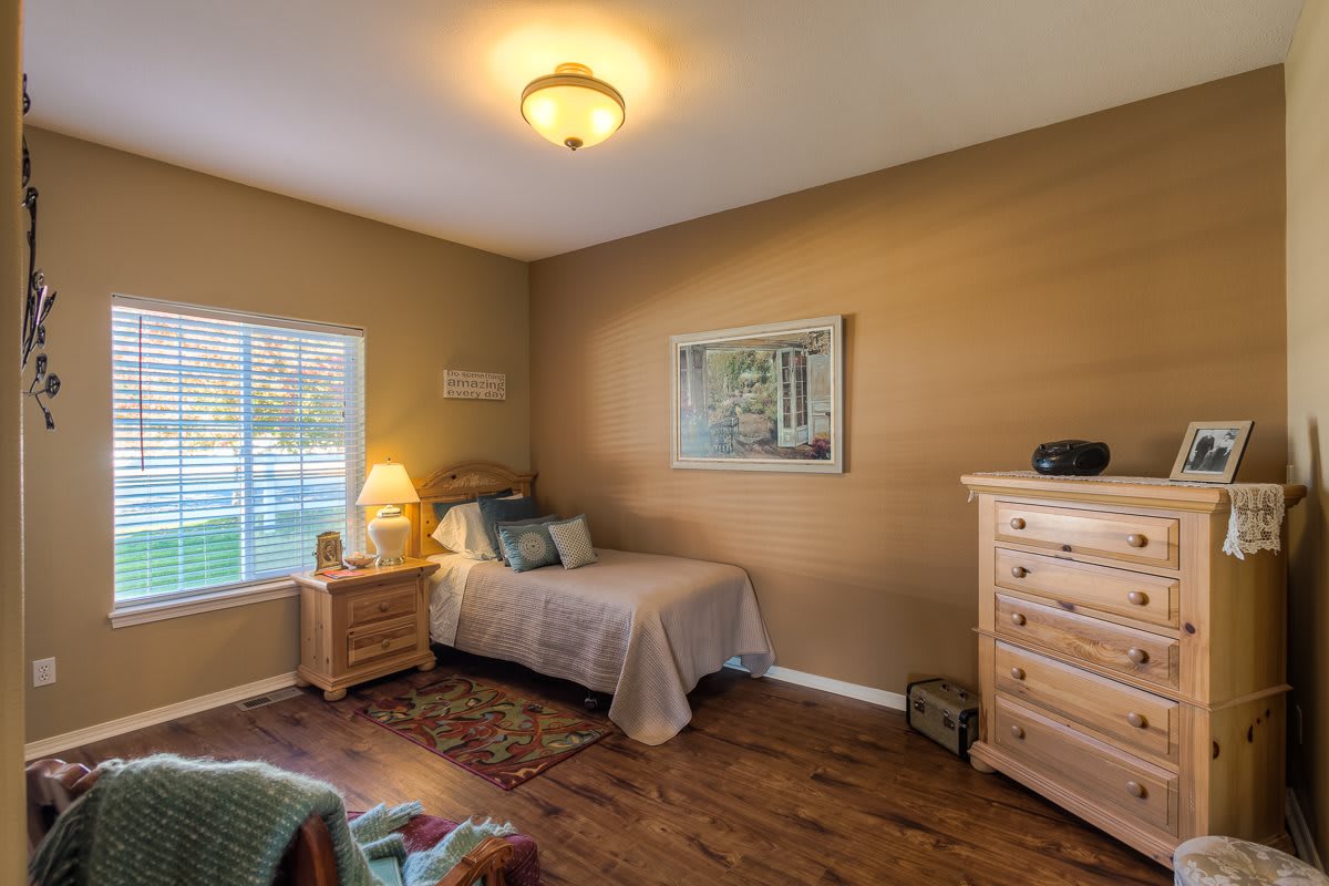 A cozy bedroom with a single bed, nightstand, and dresser, featuring warm lighting and wooden floors.