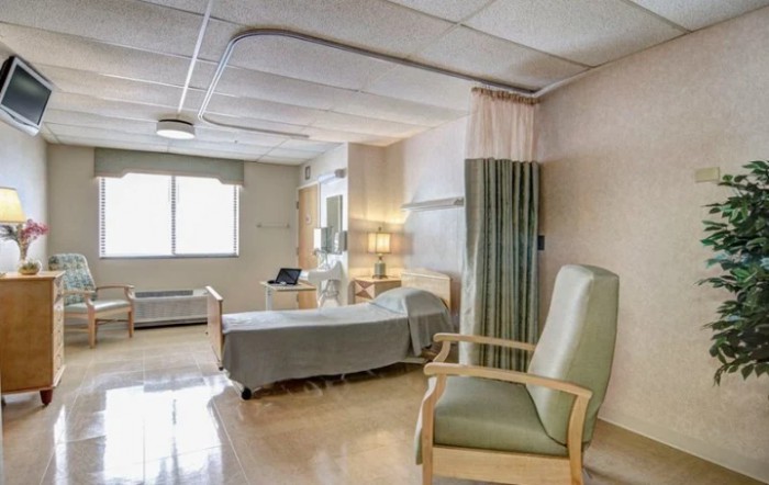 A clean and well-lit hospital room with a bed and chair, designed for patient care.