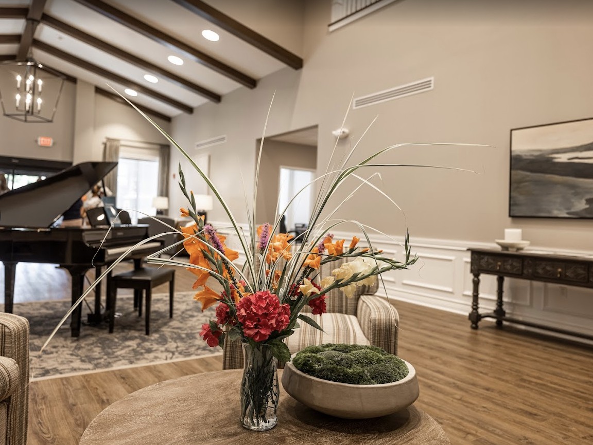 A modern living room with a high ceiling featuring elegant furniture and a vibrant floral arrangement on a wooden table.