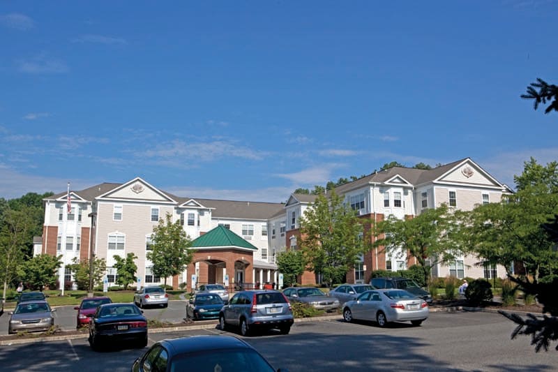 A residential building with a parking lot filled with cars under a clear blue sky.