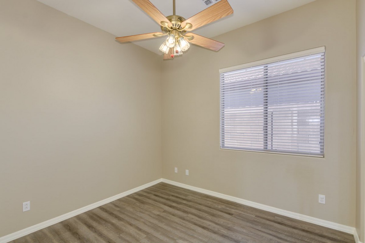 An empty room with a ceiling fan, wood flooring, and a window with blinds.