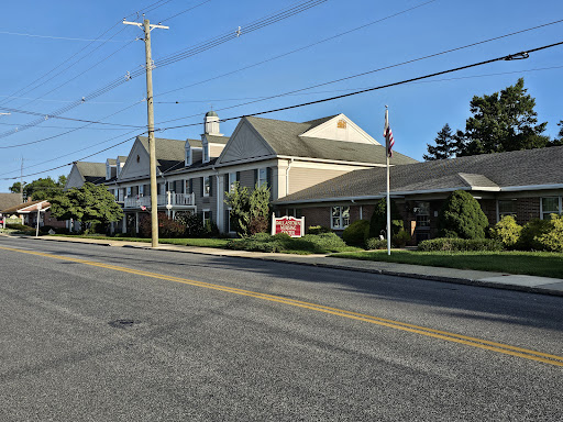 A hotel situated along a quiet street, surrounded by greenery and under a clear blue sky.