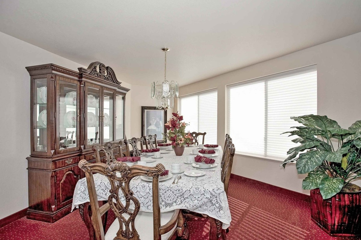 A beautifully set dining room table with ornate chairs and a china cabinet, featuring elegant decor and a plush carpet.