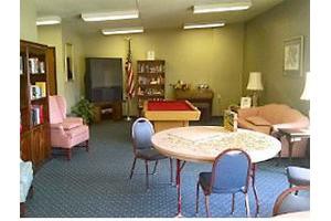 A cozy room with various furniture, including chairs, a table, a television, and a bookshelf.