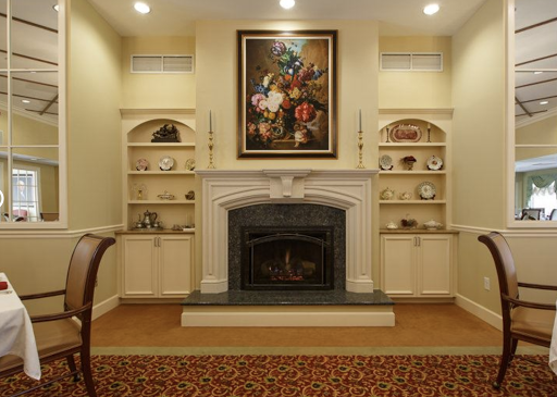 A cozy living room featuring a decorative fireplace, built-in shelves, and a beautiful floral painting.