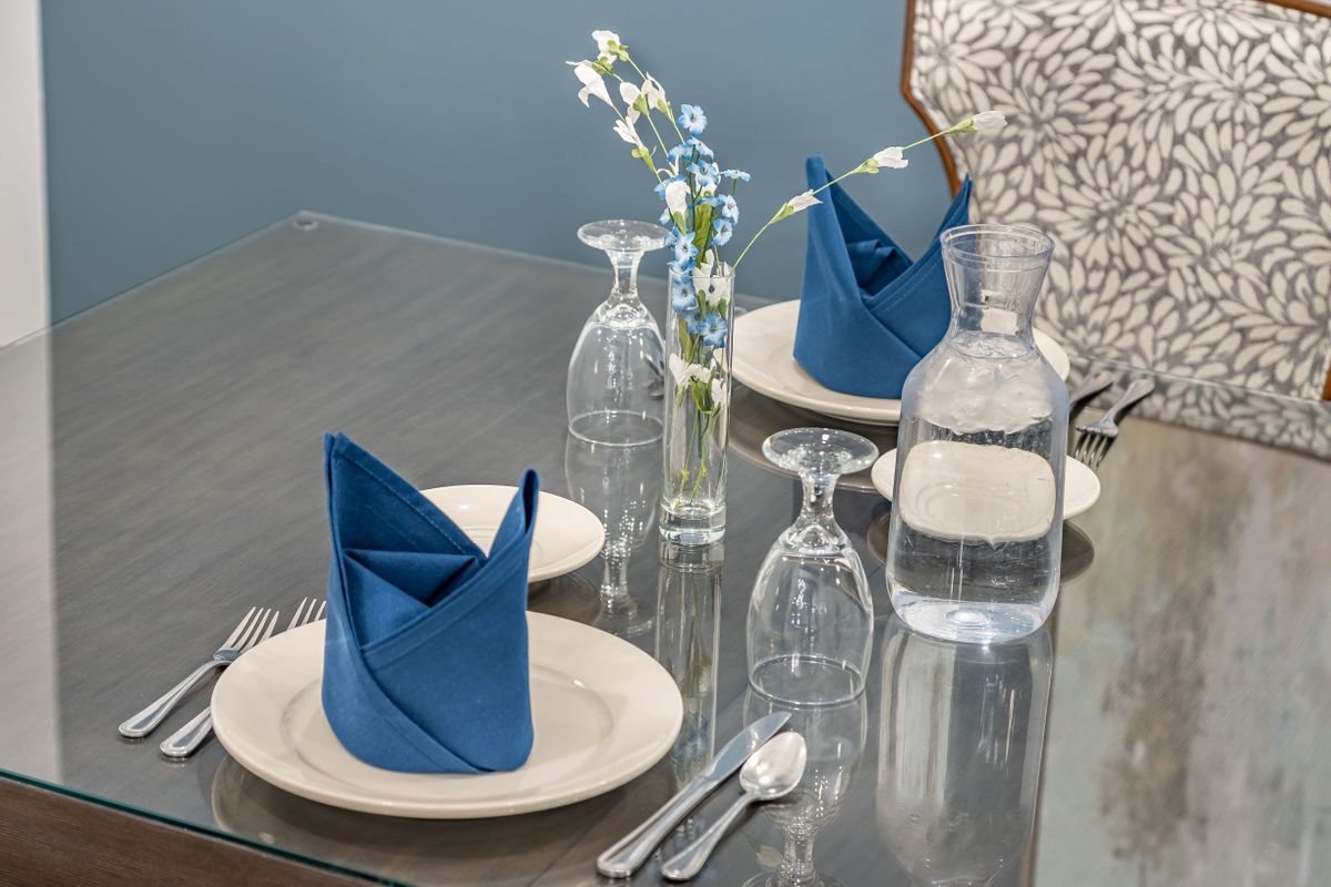 An elegantly set dining table with blue napkins, glassware, and a small vase of flowers.