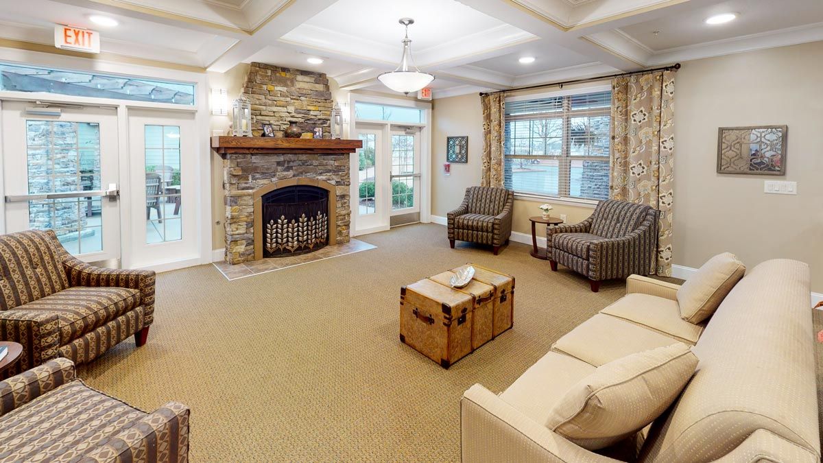 A cozy living room featuring a stone fireplace, comfortable seating, and natural light from large windows.