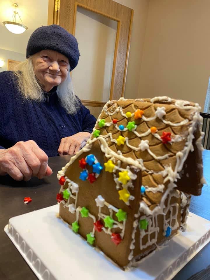 A person smiling beside their decorated gingerbread house.