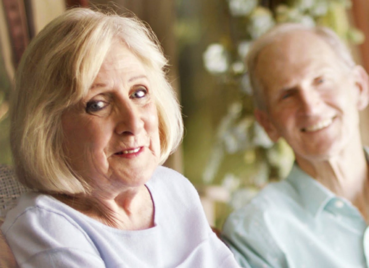 An elderly couple smiling and posing together indoors.