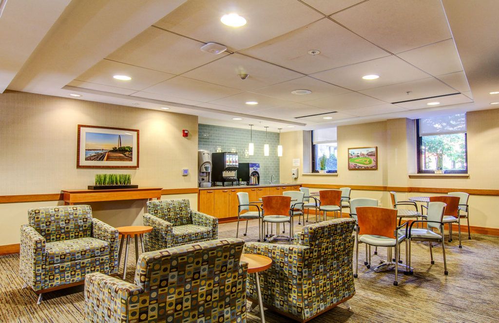 A modern and comfortable waiting area with chairs and tables, adorned with artwork and well-lit surroundings.