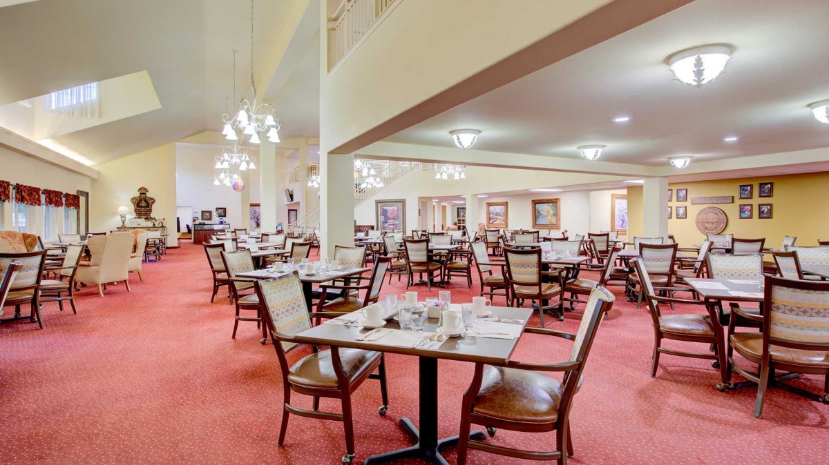 A spacious restaurant dining area with neatly arranged tables and chairs, featuring elegant lighting and a carpeted floor.