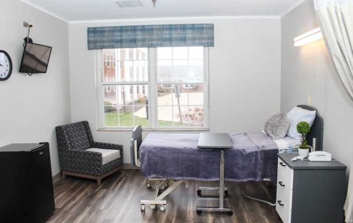 A clean and simple hospital room with a bed, chair, and window.