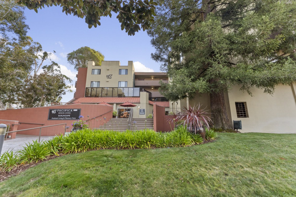 A modern residential building with well-maintained landscaping and tall trees.